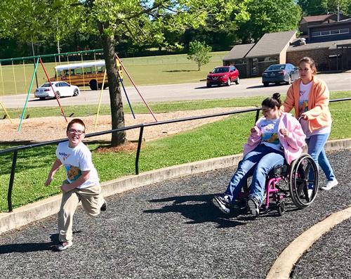 young boy runs along the track while a girl ambulates in her wheelchair 